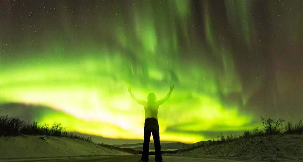A guest with arms raised under a bright green aurora