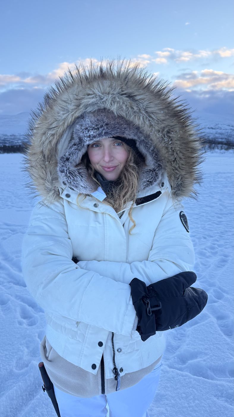 A guest smiling inside a fur-trimmed hood in the snow