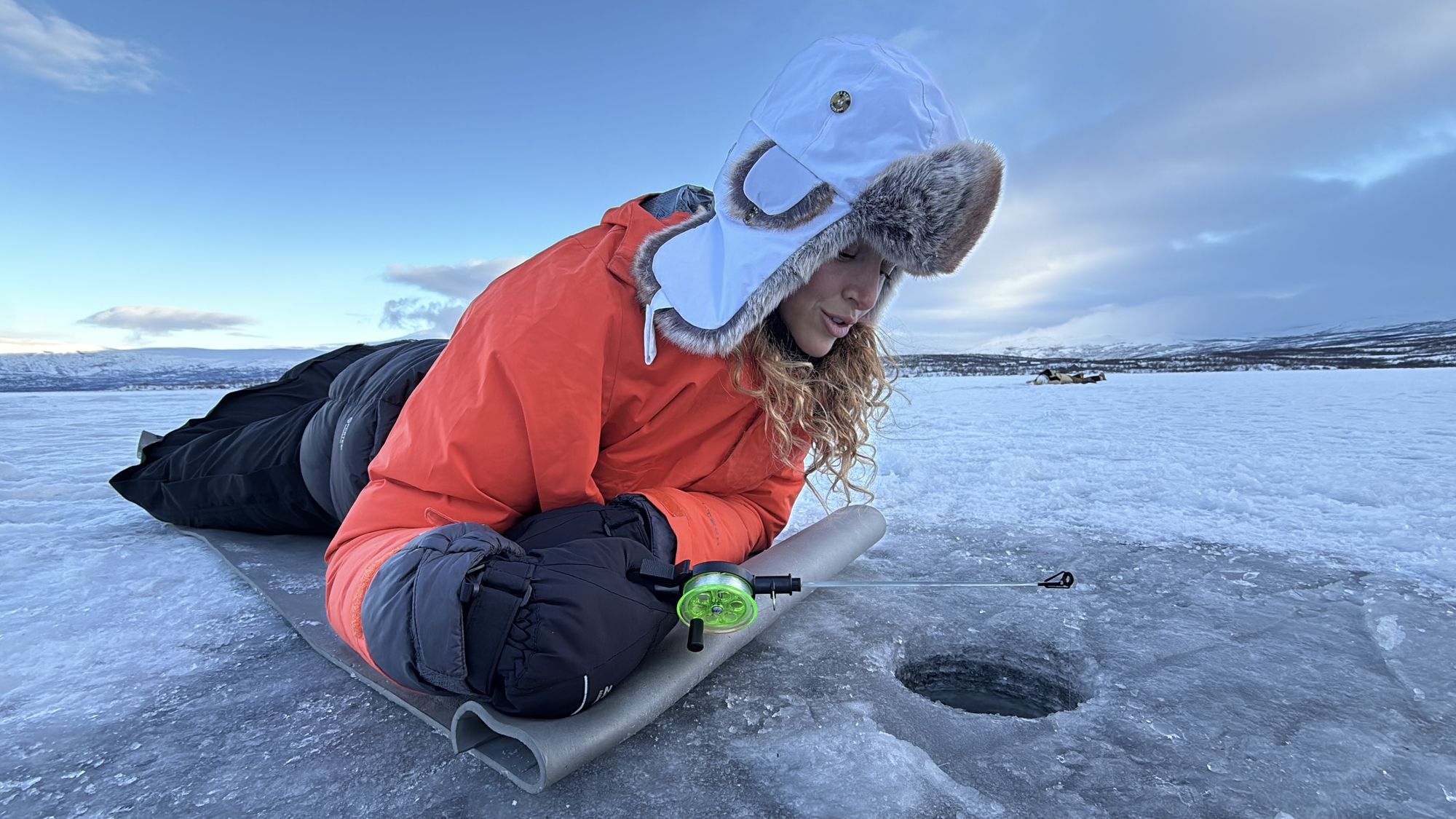 A guest lying on the frozen lake, jigging a line through the ice