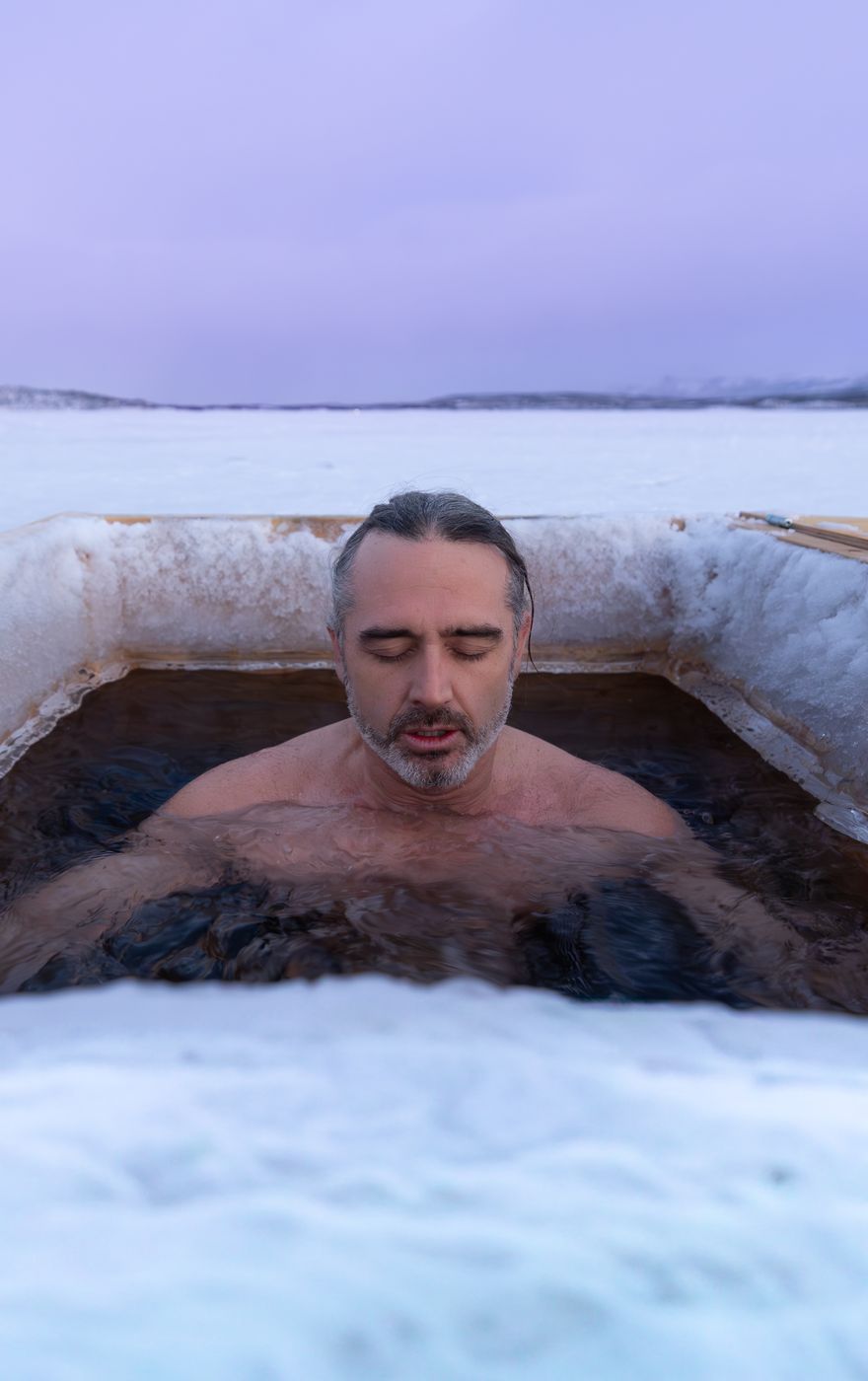 A guest sitting calmly in an ice plunge hole